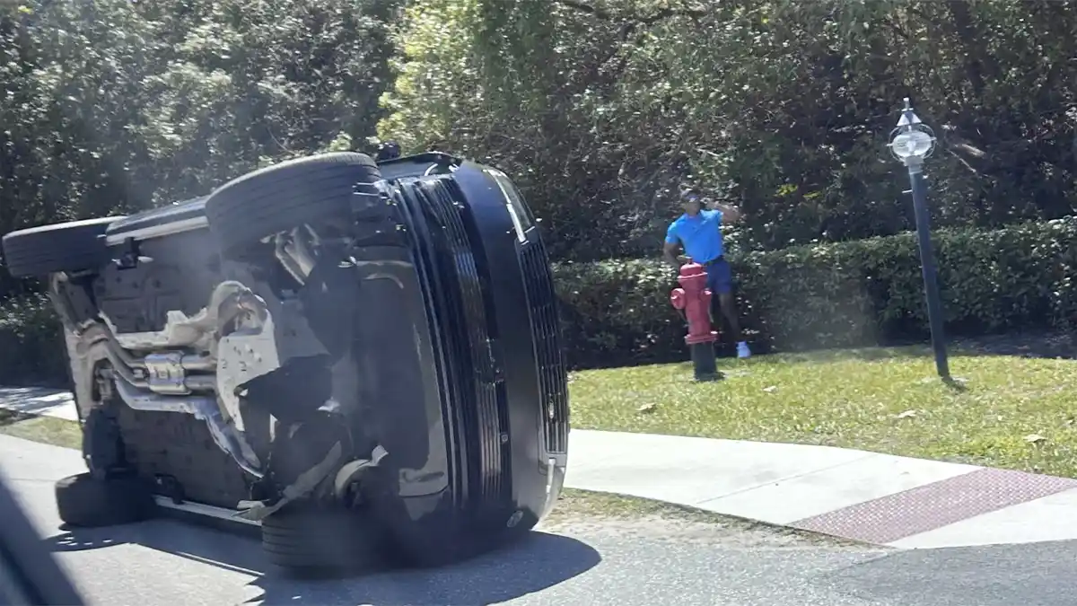 An overturned Land Rover on a Florida roadside with emergency lights in the background.